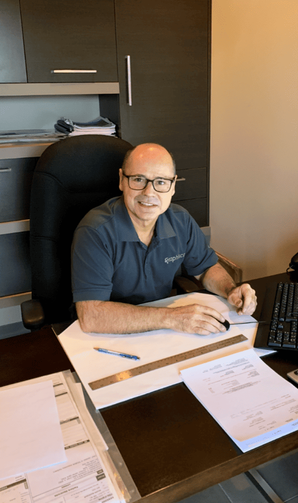 Homme souriant assis à un bureau avec des documents et un ordinateur portable