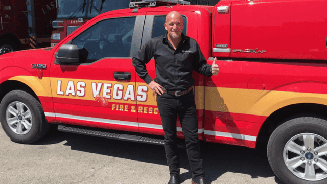 Homme debout près d'un véhicule de secours rouge marqué Las Vegas Fire & Rescue, faisant un pouce levé.