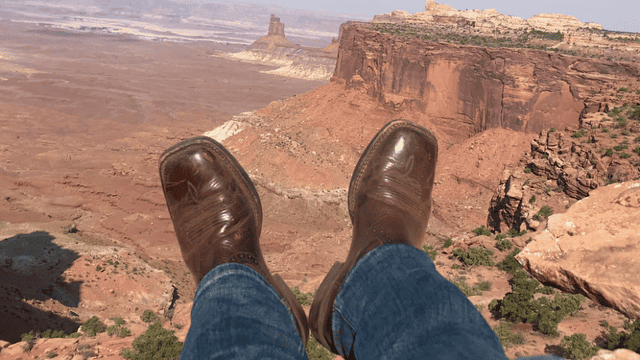 Pieds en bottes brunes suspendus au-dessus d'une falaise rocheuse dans un paysage désertique