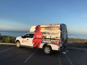 Camionnette blanche avec une carrosserie graphique rouge et blanche stationnée près d’un littoral au coucher du soleil